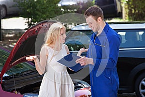 Mechanic showing clipboard to angry woman by breakdown car