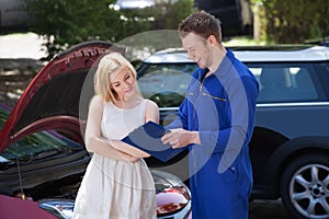 Mechanic showing clipboard to customer by breakdown car