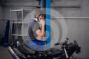 Mechanic sitting on a bike and talking on the phone