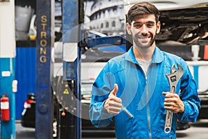 Mechanic standing and hold a wrench with blur garage in the background. Auto car repair service center. Professional service