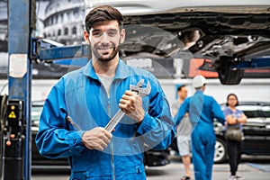Mechanic standing and hold a wrench with blur his assistant talking with customers in the background. Auto car repair service.