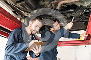 Mechanic Taking Notes While Coworker Repairing Car