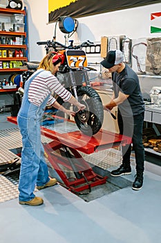 Mechanic team adjusting motorbike wheel on factory