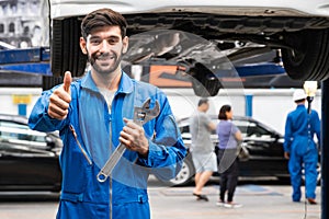 Mechanic thumb up standing and hold a wrench with blur garage in the background. Auto car repair service center.