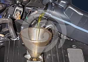 Mechanic topping up the oil in a car pouring a pint of oil through a funnel into the engine, close up of the oil and funnel