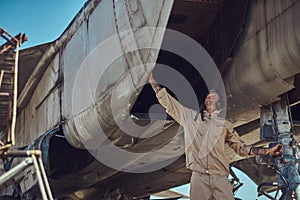 Mechanic in uniform carries out maintenance of a war fighter-interceptor in an open-air museum.