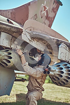 Mechanic in uniform and flying helmet repair old war fighter-interceptor in an open-air museum.