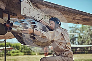 Mechanic in uniform and flying helmet repair old war fighter-interceptor in an open-air museum.