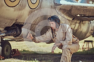 Mechanic in uniform and flying helmet repair old war fighter-interceptor in an open-air museum.
