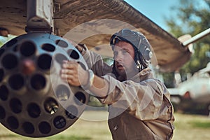 Mechanic in uniform and flying helmet repair old war fighter-interceptor in an open-air museum.