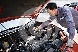 A mechanic in uniform and protective glove looks at a sport car's engine to fix it. Working atmosphere at car repair shop