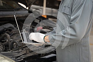 Mechanic using a laptop computer to check collect information during work a car engine. service maintenance of industrial to