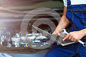 Mechanic Using Laptop While Examining Car Engine