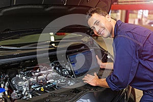 Mechanic Using Laptop While Examining Car Engine