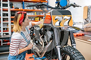 Mechanic woman cleaning motorcycle with cloth and polish on factory