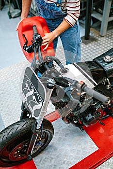 Mechanic woman with jerry can filling fuel tank of motorcycle on factory