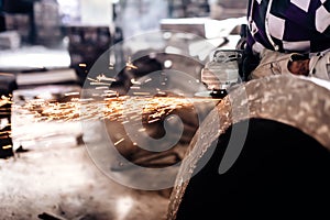 Mechanic worker using grinder for polishing an iron block