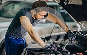 Mechanic working under car hood in repair garage