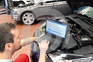 Mechanic in a workshop checks and checks the electronics of the car - software update with a modern computer