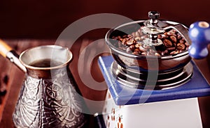 Mechanical coffee grinder, old copper cezve and coffee beans. Over wooden table as background.