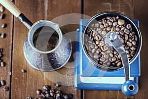 Mechanical coffee grinder, old copper cezve and coffee beans. Over wooden table as background.