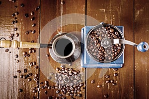 Mechanical coffee grinder, old copper cezve and coffee beans. Over wooden table as background.