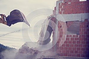 Mechanical digger demolishing the wall of a brick building photo