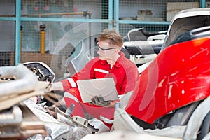 Mechanical man inspecting car parts stock on laptop computer while working in garage warehouse, Young mechanic with laptop in auto