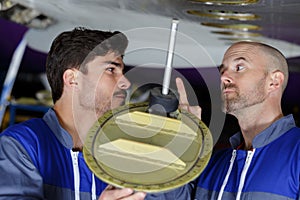 mechanics inspecting aircrafts undercarriage apprentice receiving warning from supervisor