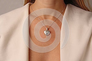 Medallion pendant in shape of heart made of silver on chain hangs around neck, on chest of a young girl. Love and romance,