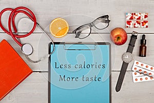 clipboard with text & x22;Less calories more taste& x22;, book, pills, eyeglasses, watch, fruit and stethoscop