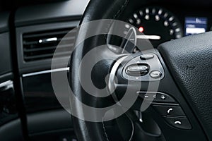 Media control buttons on the steering wheel in black perforated leather interior with computer monitor. Modern car interior detail