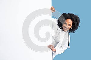Medical ad and offer. Smiling black millennial woman doctor in white coat with banner with copy space