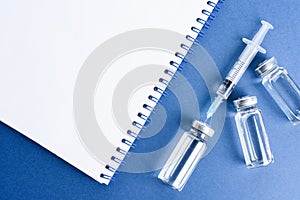 Medical ampoule with vaccine and journal for records on blue background