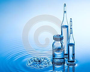 Medical ampoules and botttle on the blue water background with splash