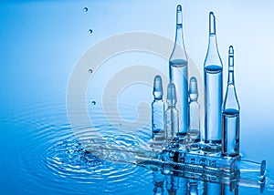 Medical ampoules and syringe on blue water background with splash and drops