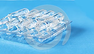 Medical ampoules on the table in transparent packaging on a blue background. Medical glass ampoules