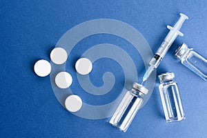 Medical ampoules with vaccine and pills on a blue background.