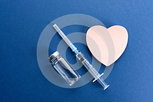 Medical ampoules with a vaccine and a sticker in the form of a heart on a blue background.