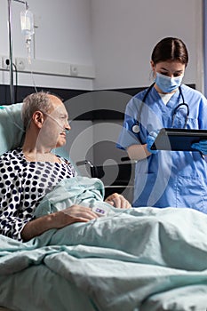 Medical assistant with protection mask checking treatment of senior man