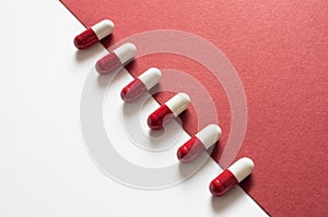 Medical background, red-white capsules on a red-white background. Top view of row of pills on halved white and red surface