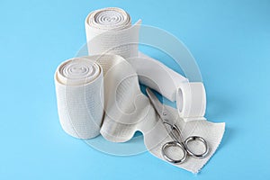 Medical bandage rolls, sticking plaster and scissors on light blue background