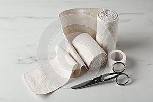 Medical bandage rolls, sticking plaster and scissors on white wooden table