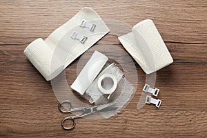 Medical bandage rolls, sticking plaster and scissors on wooden background, flat lay