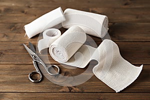 Medical bandage rolls, sticking plaster and scissors on wooden table