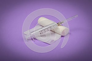 Medical bandage and syringe on a lilac background. A gauze roll on which the syringe lies. Dressing for medical purposes.