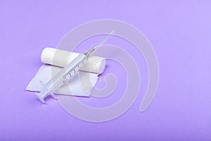 Medical bandage and syringe on a lilac background. A gauze roll on which the syringe lies. Dressing for medical purposes. Space