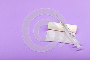 Medical bandage and syringe on a lilac background. A gauze roll on which the syringe lies. Dressing for medical purposes. Space