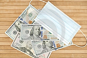 A medical blue mask lies on dollars with a face value of 100 dollars on a wooden background. 100 dollar bill and protection