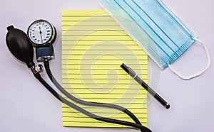 medical blue mask with notepad pen and manual blood pressure reader on white background flat lay representing work of doctors